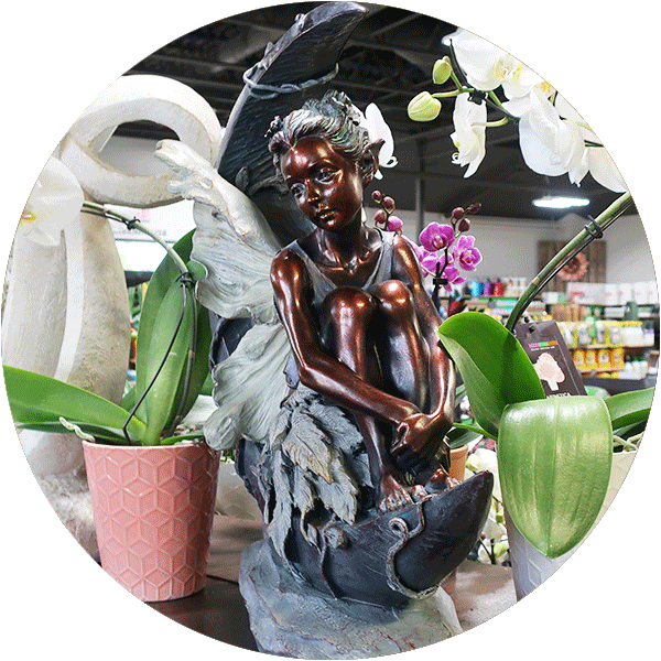 A fairy statue sitting next to a few houseplants.